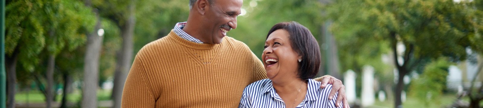 a mature couple laughing while walking in a park.