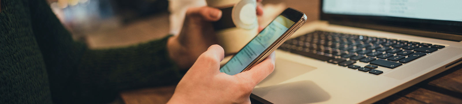 a person viewing their mobile phone while holding a cup of coffee